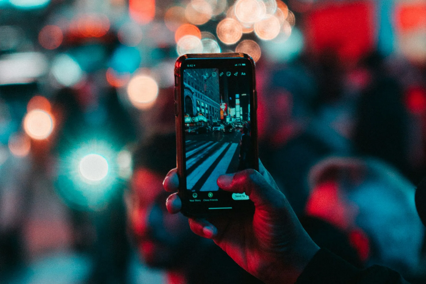 A phone held up to photograph a street washed in teal and red neon