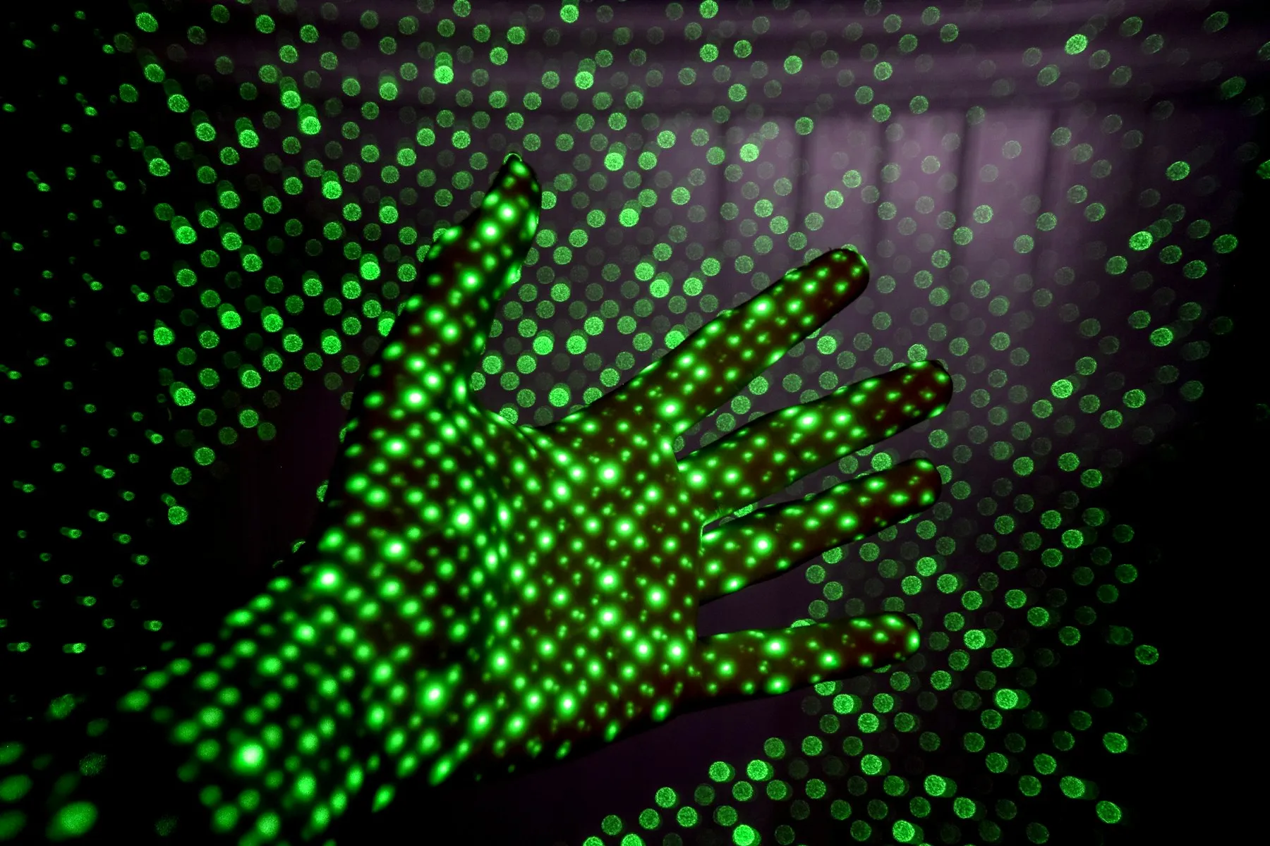 A hand lit by a dense grid of bright green LEDs