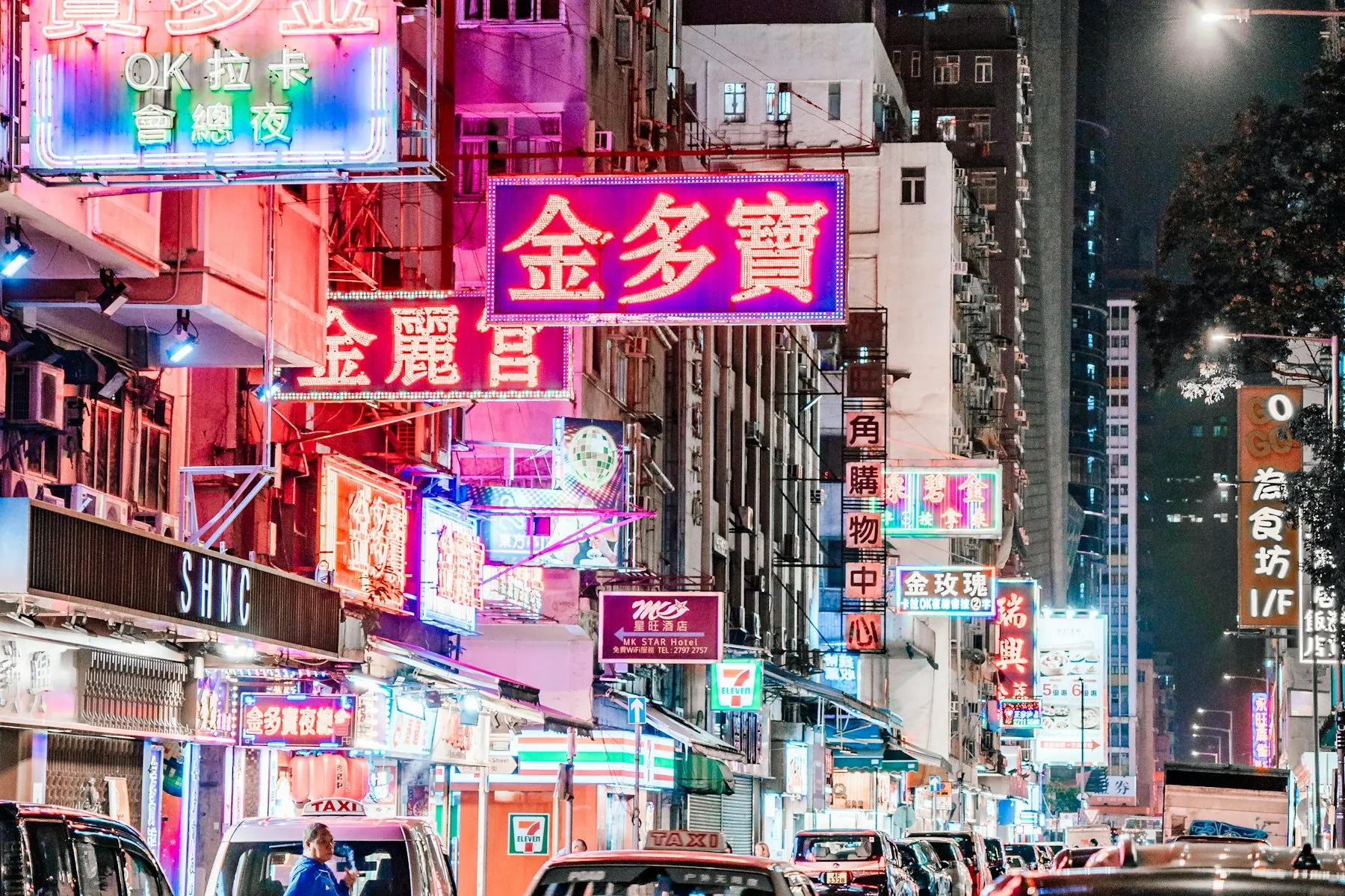 A city street at night under stacked pink and magenta neon signs