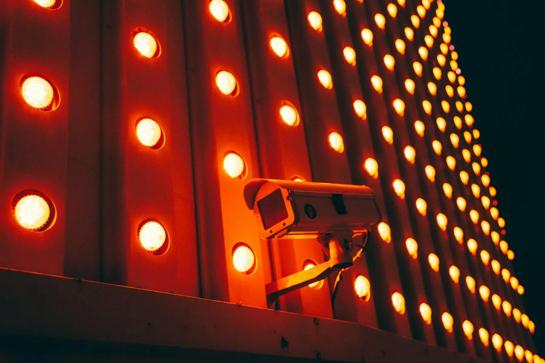A surveillance camera in front of a wall of glowing red and orange lights