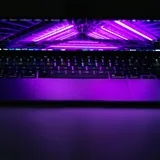 A laptop keyboard and screen glowing under purple backlight