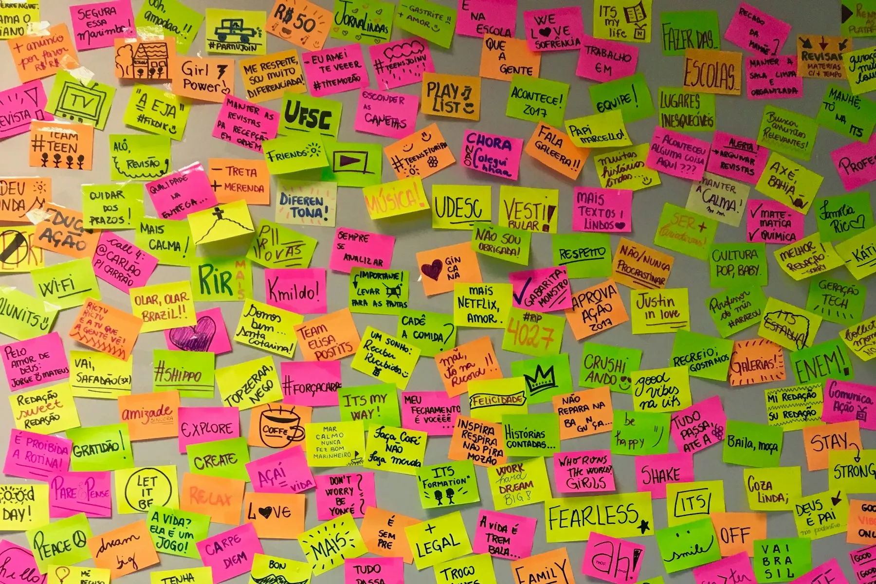 A wall densely covered in pink, yellow and green sticky notes