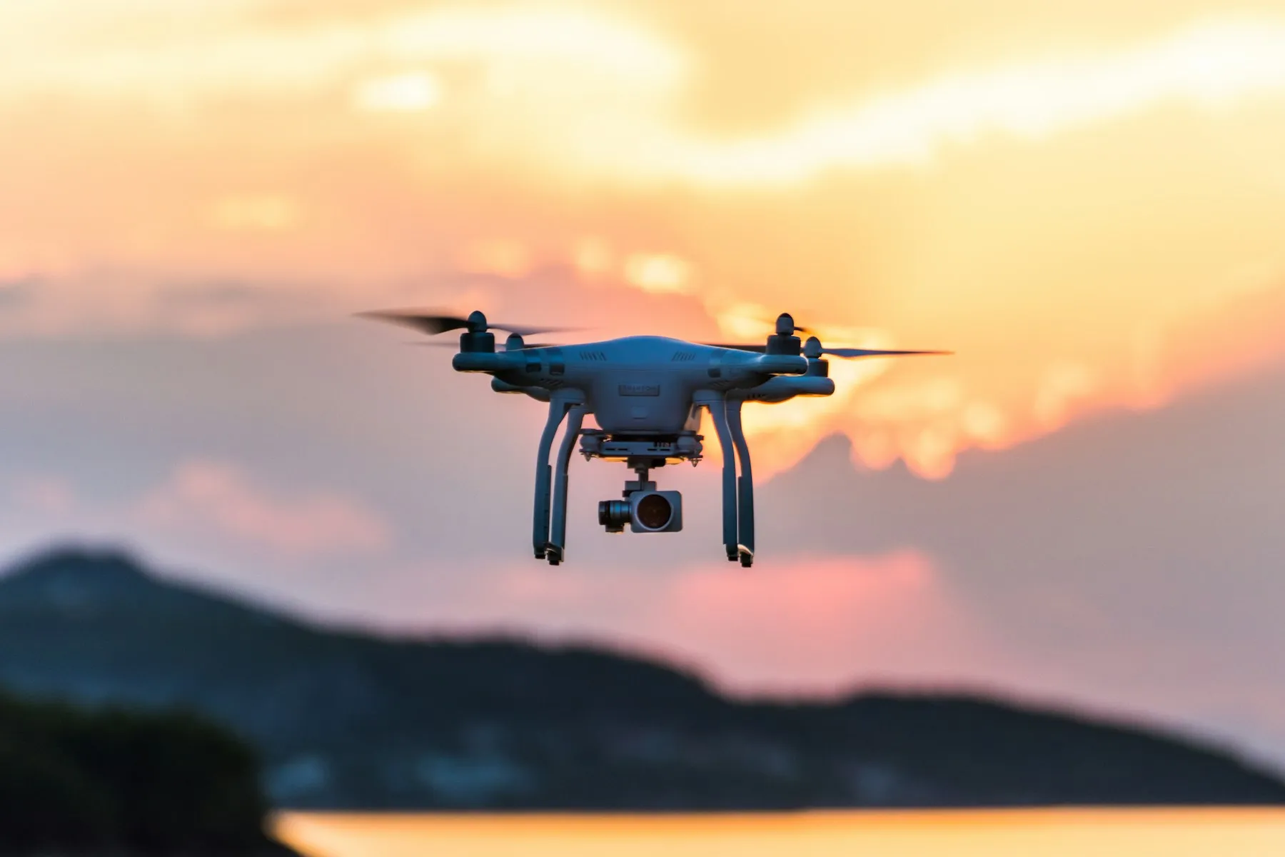 A quadcopter drone hovering against a pink and orange sunset sky