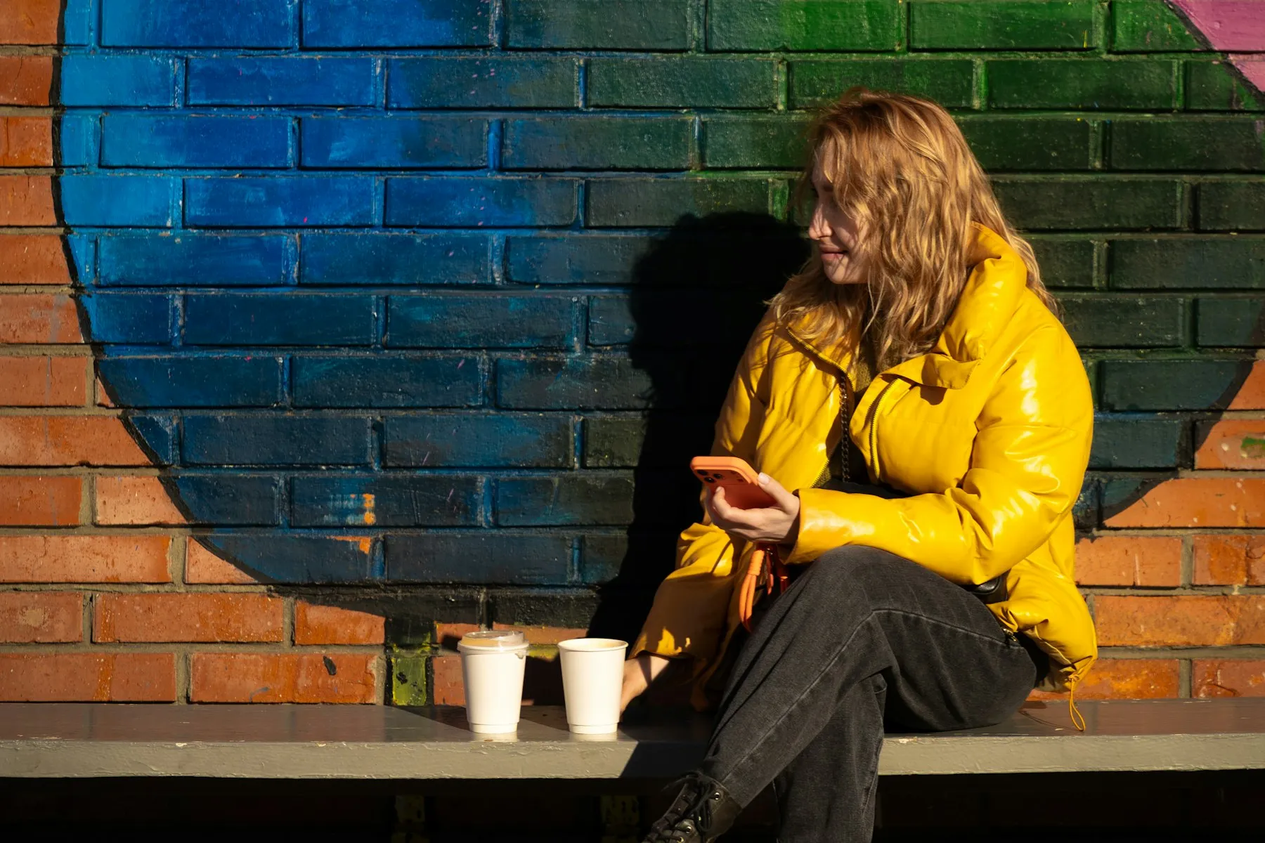 A person in a bright yellow jacket sitting against a painted blue and orange wall