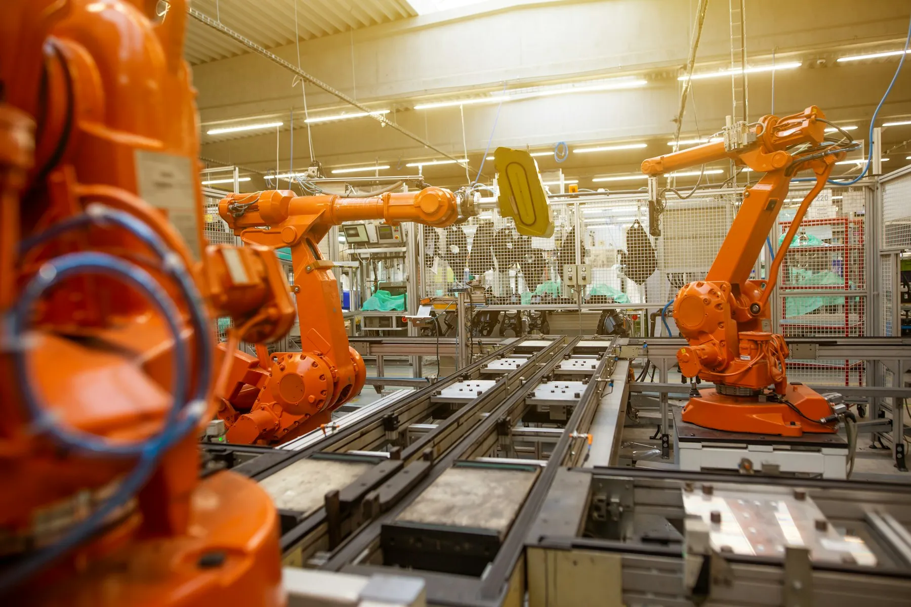 A row of bright orange industrial robot arms on a factory floor